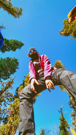 Low angle view of woman against trees against clear blue sky