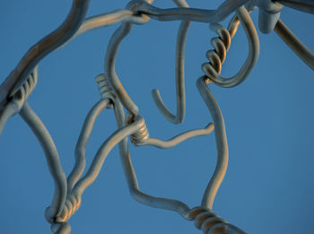 Low angle view of metallic wire against clear blue sky