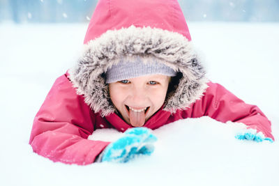 Girl sticking out tongue while lying on snow covered land
