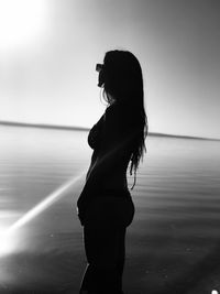 Side view of woman standing in sea against sky