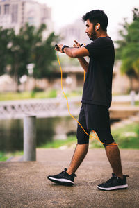 Man using jumping rope outdoors and looking at his smart watch.