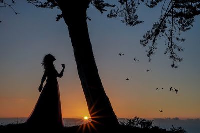 Silhouette woman by statue against sky during sunset