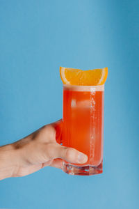 Cropped hand holding drink against blue background