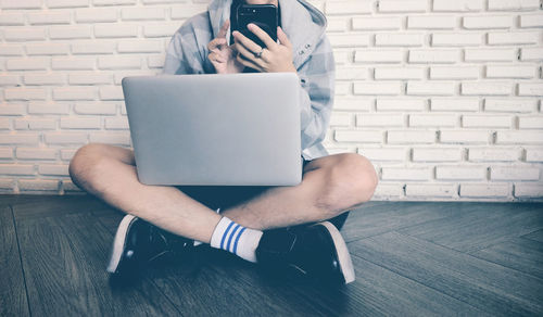 Midsection of man using mobile phone while sitting on wall