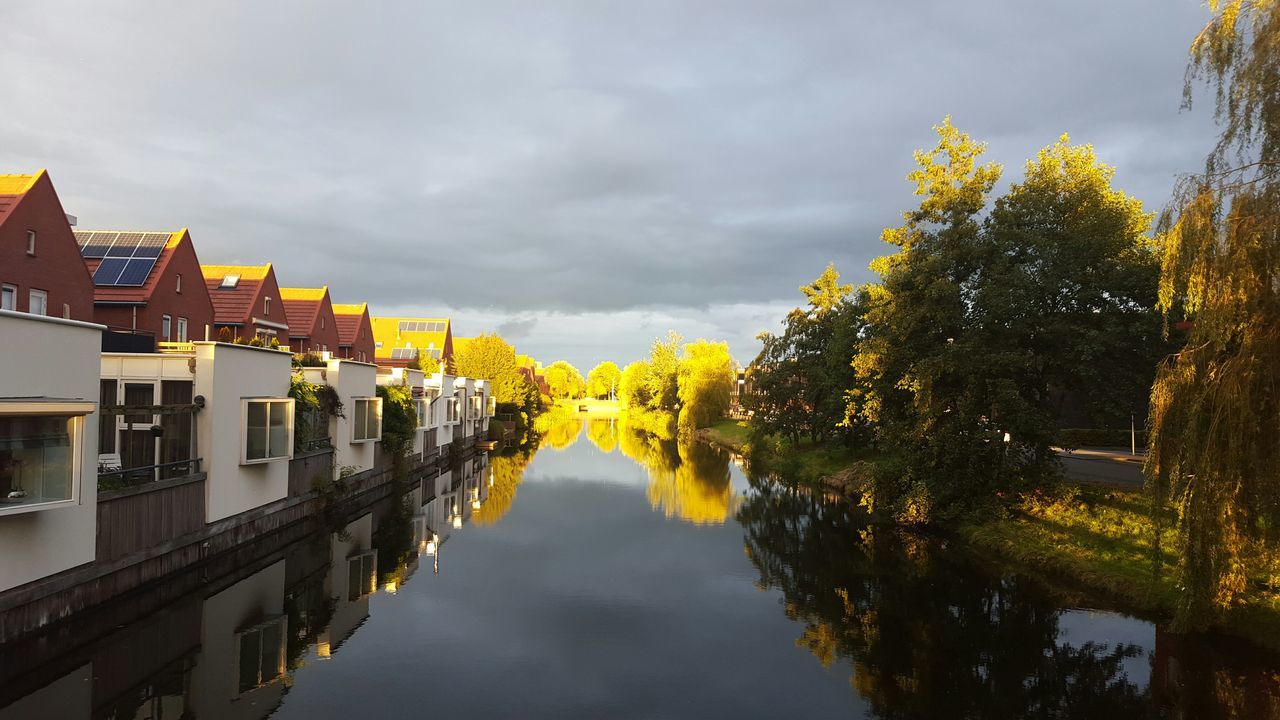 water, sky, reflection, waterfront, architecture, built structure, cloud - sky, canal, building exterior, tree, river, nature, yellow, beauty in nature, cloud, cloudy, tranquility, standing water, weather, outdoors