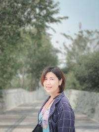 Portrait of smiling young woman standing against trees