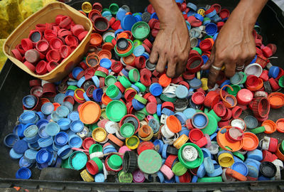 Cropped hands with colorful bottle caps in container