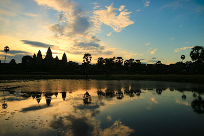 Silhouette buildings by lake against sky during sunset