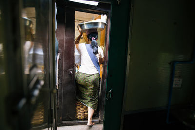 Rear view full length of female vendor carrying container in train