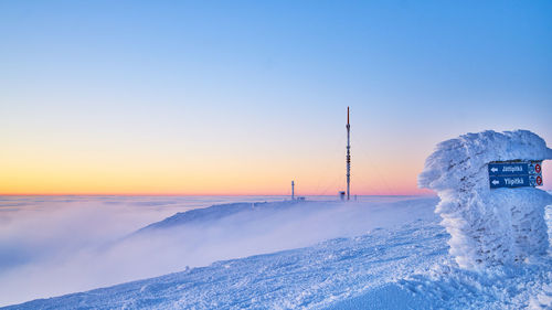 Information sign on snow covered land against clear sky during sunset