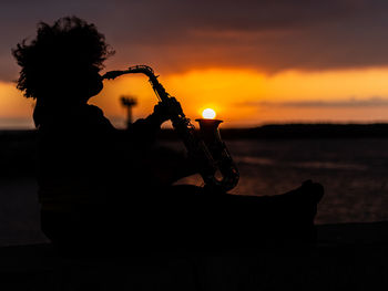 Silhouette woman sitting on stage against sky during sunset