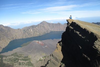 Man sitting on mountain against cloudy sky