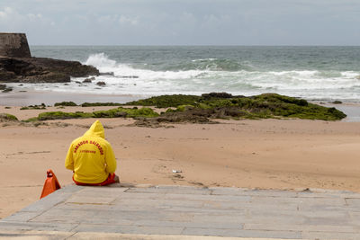 Rear view of lifeguard sitting on jetty at beach