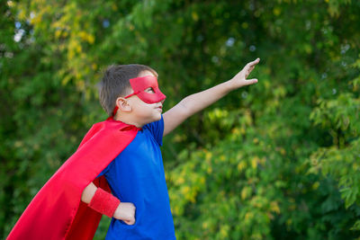 Boy in superman costume standing against tree