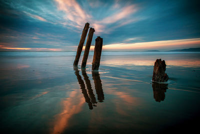 Wooden posts on sea against sky during sunset