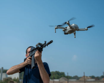 Low angle view of man holding drone flying against sky