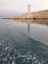 Lighthouse on sea by buildings against sky