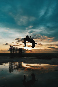 Man in mid-air reflecting on puddle during sunset