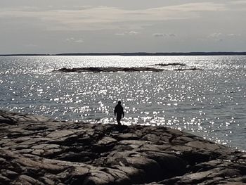 Silhouette man standing on rock by sea against sky