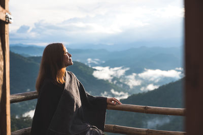 Smiling woman standing by railing in balcony against mountains