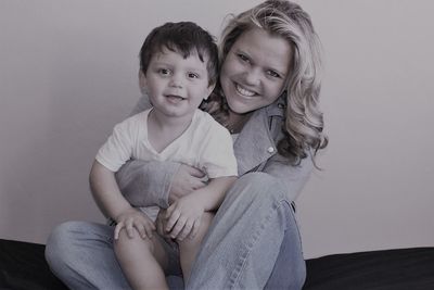 Portrait of happy son sitting on mother lap at home