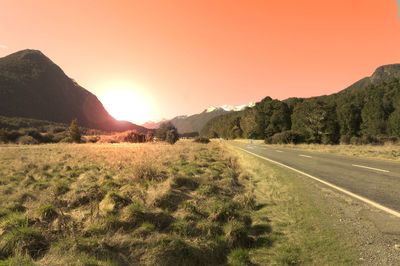 Road by landscape against sky during sunset