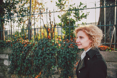 Side view of smiling young woman standing against fence