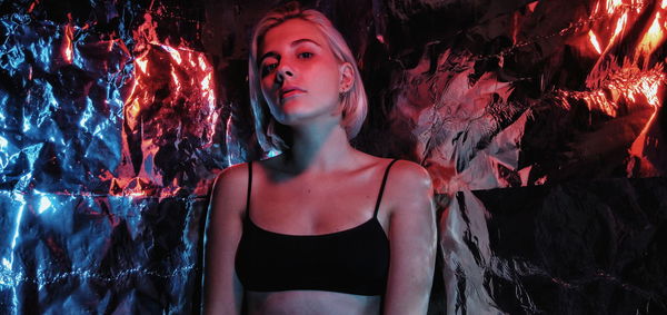 Portrait of young woman standing against illuminated wall