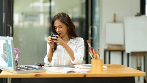 Young woman using mobile phone while sitting on table