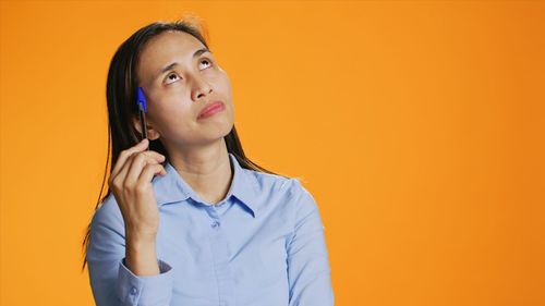 Portrait of young woman standing against yellow background