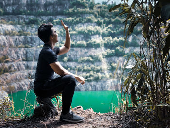 Side view of man gesturing against pond in forest