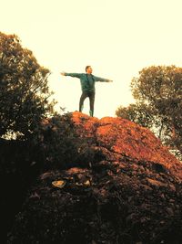 Low angle view of young woman standing on rock against sky