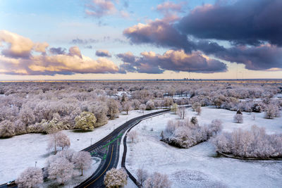 Road by snow covered landscape against sky during sunset