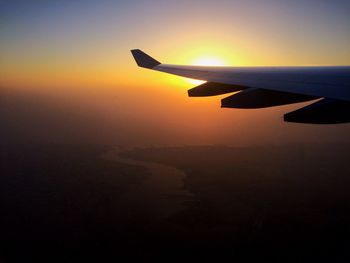 Airplane wing against sky during sunset