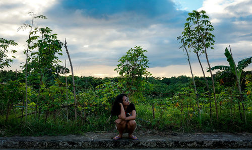 Full length of woman crouching on field against sky