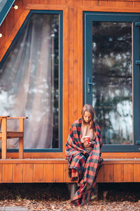 Full length of woman sitting against house