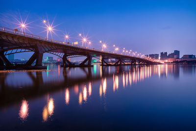 Illuminated bridge over river against sky in city at night