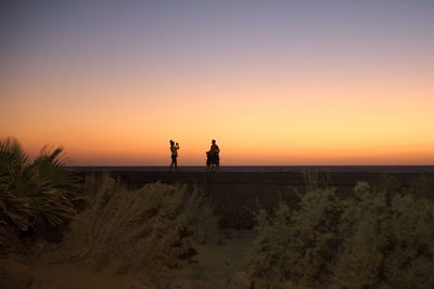 Silhouette people on beach against clear sky during sunset