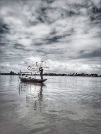 Silhouette mature man fishing in sea while standing on boat against cloudy sky