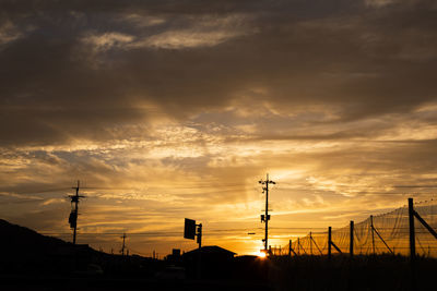Silhouette of electricity pylons against dramatic sky