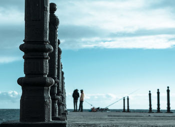 Rear view of friends on pier over sea against cloudy sky