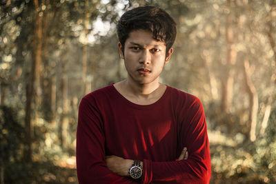 Portrait of young man with arms crossed standing against trees in forest
