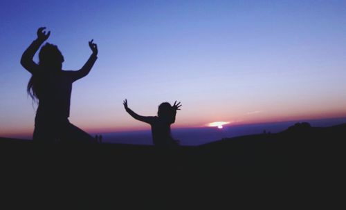 Silhouette man and woman dancing against sky during sunset