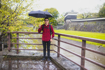 Portrait of man with umbrella standing on bridge during rainy season