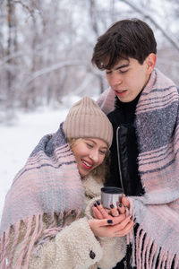 Young couple with coffee cup embracing outdoors during winter