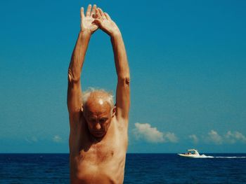 Shirtless senior man exercising by sea against sky