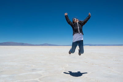 Girl jumping at salinas grandes against blue sky