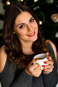 Portrait of young woman having coffee against christmas tree at home