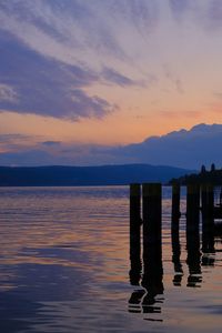 Wooden posts in sea against sky during sunset