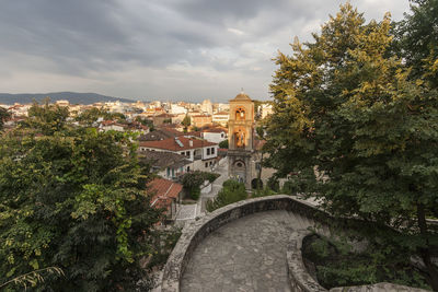 Arch bridge amidst trees and buildings against sky